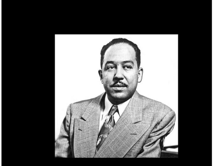 Black-and-white portrait of Langston Hughes, mid-life, in a light double-breasted suit, looking directly at the camera with a composed half-smile.